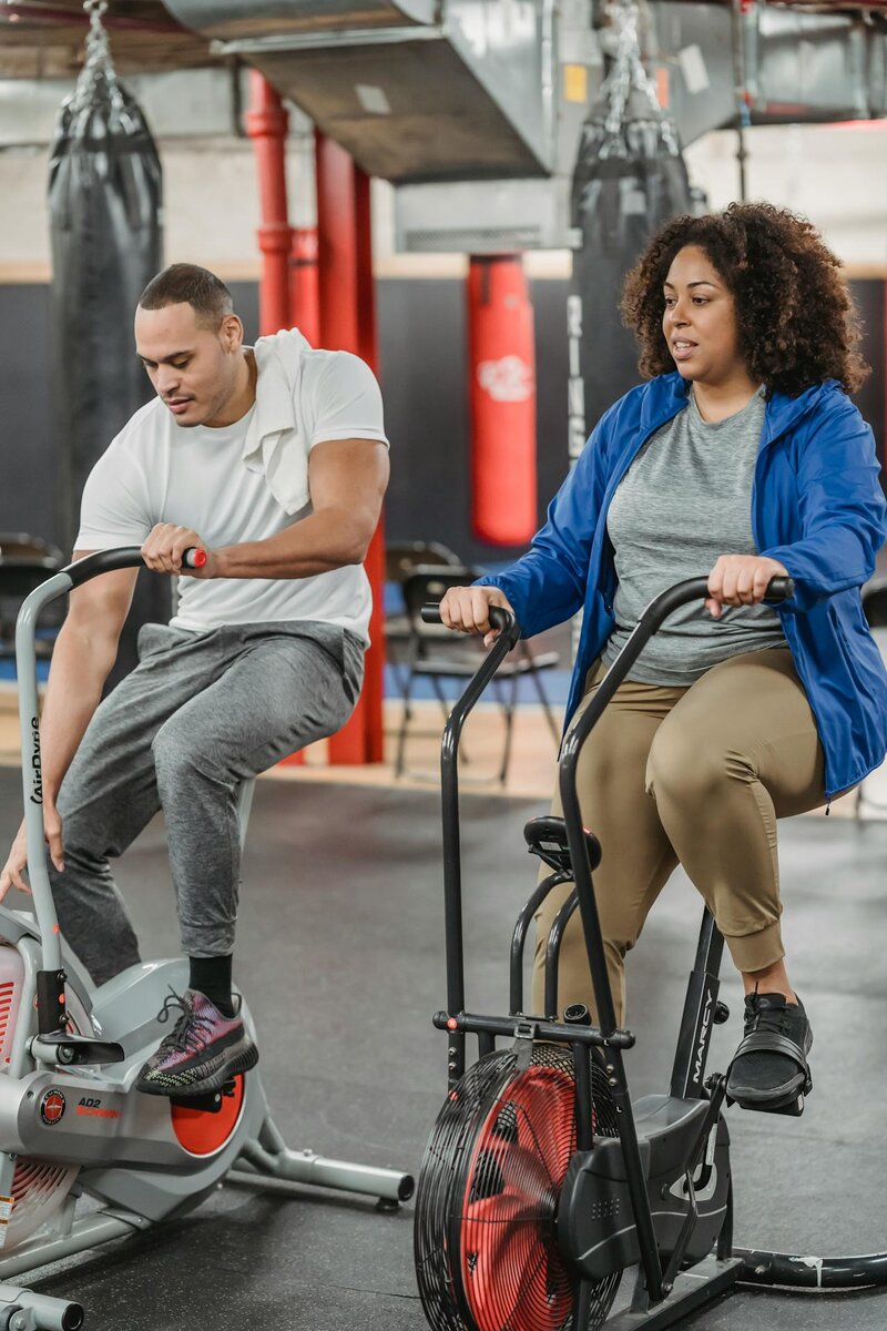 Two people doing stationary cycling exercise on a gym bike with correct sitting posture